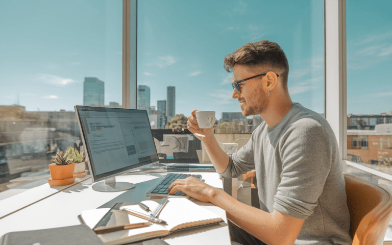 Jeune rédacteur web concentré dans un espace de coworking moderne et lumineux, son bureau équipé d'un ordinateur portable, d'un carnet et d'une tasse de café, avec vue sur une ville animée.