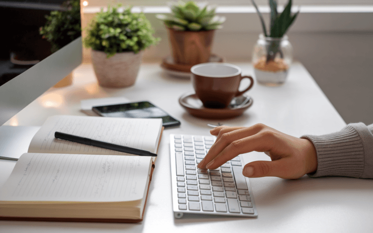 Main tapant sur un clavier d'ordinateur pour créer un blog, entourée d'un carnet, d'un stylo, et d'une tasse de café, dans une ambiance chaleureuse.