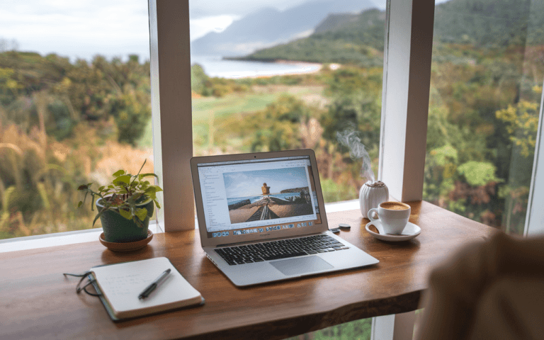 Créer un blog : espace créatif sur une table en bois avec ordinateur ouvert sur blog de voyage, carnet de notes, appareil photo et café, vue nature inspirante.
