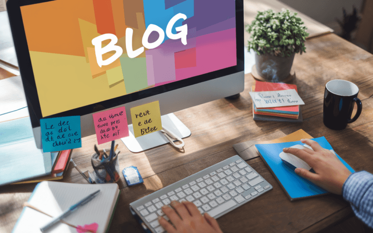 Un bureau professionnel avec clavier d'ordinateur et écran affichant une interface moderne de création de blog, entouré d'un carnet de notes, stylo, tasse de café et post-it inspirants, symbolisant créativité et motivation.